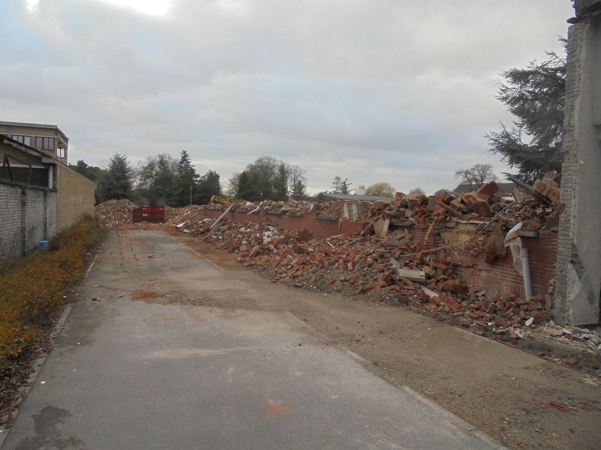 Puin van een afgebroken gebouw langs een weg, met een container verderop