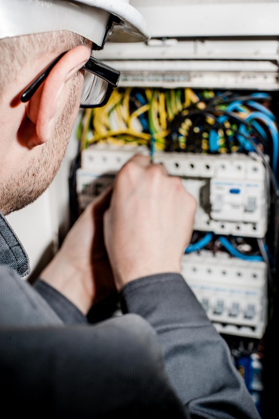 Een elektricien met helm werkt aan de automaten in een zekeringkast