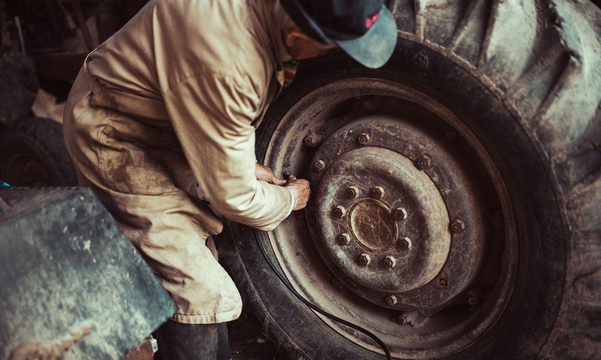 Iemand werkt aan het wiel van een tractor in een loods