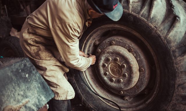 Iemand werkt aan het wiel van een tractor in een loods